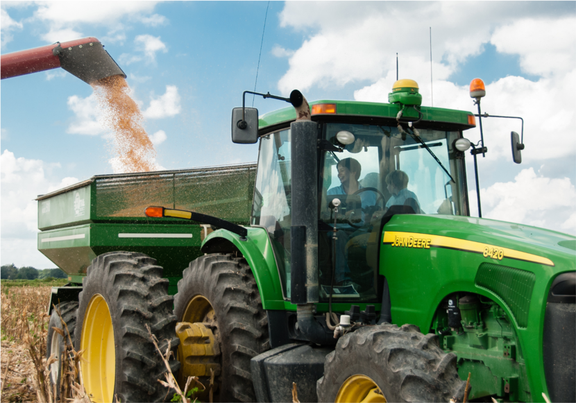 Tractor op een akker met aanhangwagen en een andere machine spuit de geoogste teelt in de aanhangwagen