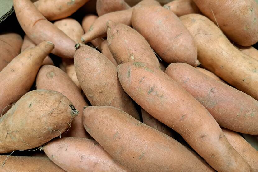 A stack of sweet potatoes can be seen up close in a paper crate.