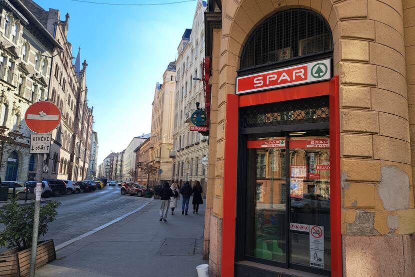 The front door and sign of a small Spar chain grocery store can be seen, on the corner of an old residential building in downtown Budapest.