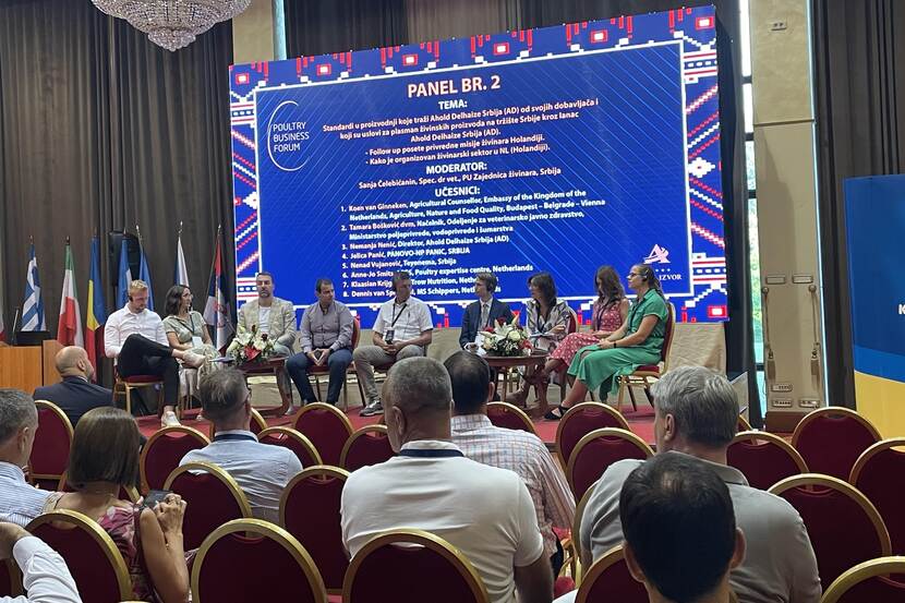 A group of experts sit on chairs on a stage. There is a slide projected behind them. It's a professional panel in front of an audience.