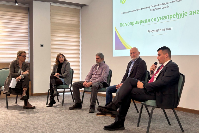 Expert speakers sit on chairs in front of a slide from a presentation. The slides have texts written on them in Serbian Cyrillic. The experts are talking about soil health.